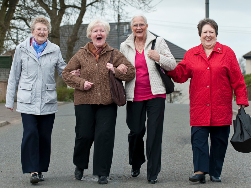 4 older women walking together arm in arm